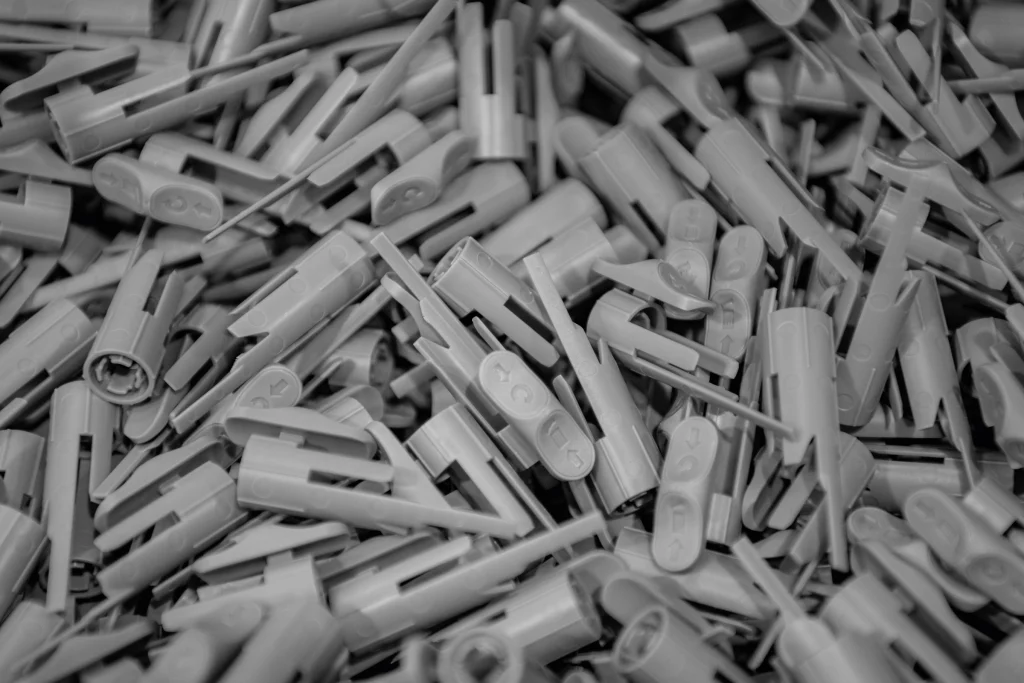 Close-up of a large pile of grey injection-moulded plastic components used in medical device manufacturing, showing precision detail of the moulded parts.